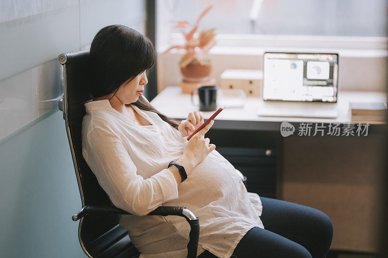 an asian chinese pregnant woman working from home during the lock down checking on her message using her phone taking a break in her home office